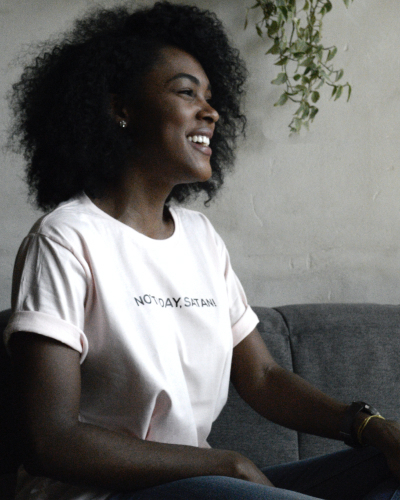 A woman of colour in a white T-shirt smiles, looking off camera